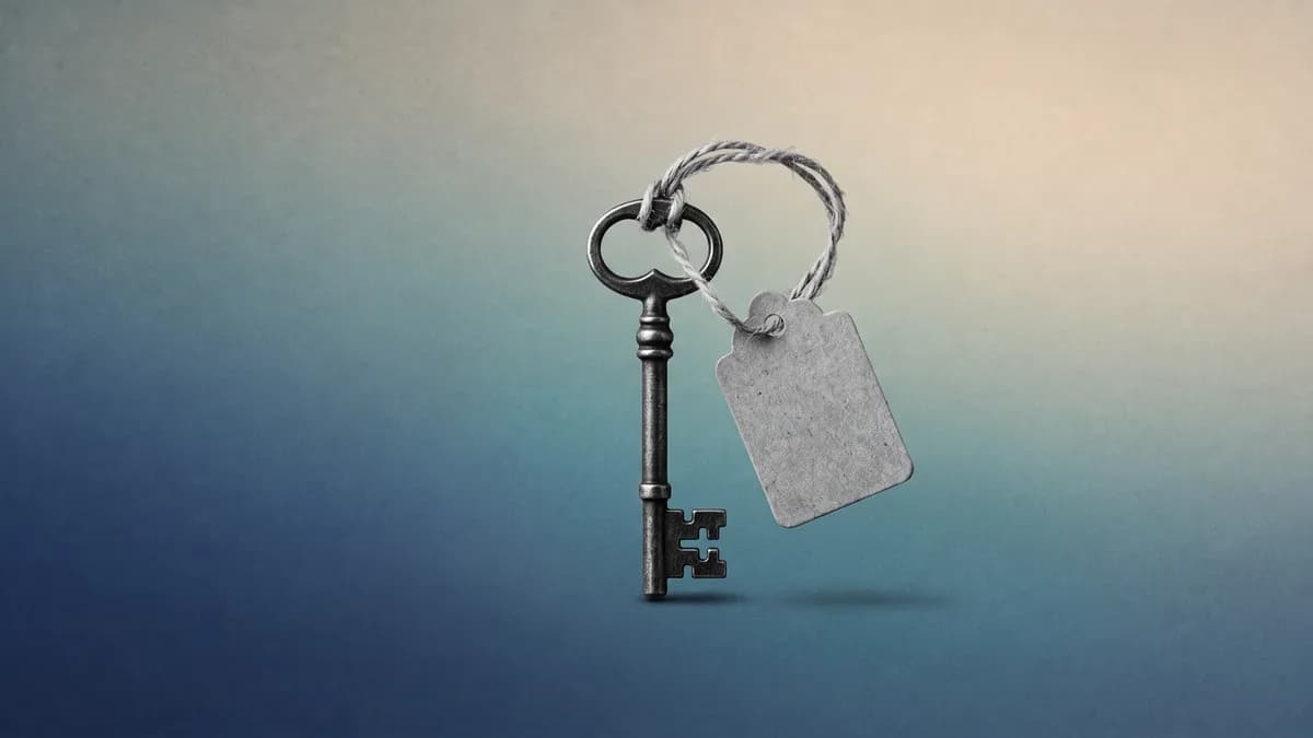 Llave antigua de metal con una etiqueta de cartón en blanco atada con hilo, en blanco y negro sobre un fondo degradado azul petróleo, verde azulado y crema